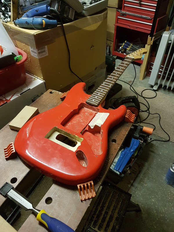 A half-finished guitar. A piece of teak wood lies next to it.